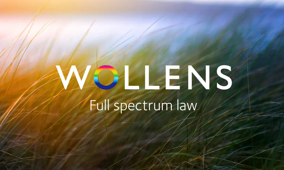 An image of dune grass slightly blurred with the Wollens company logo in the foreground