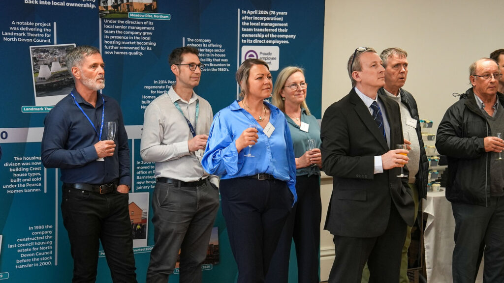 PR Pearce A group of people listening to a person speaking whilst holding drinks at an event