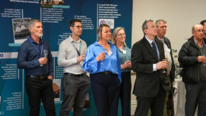A group of people listening to a person speaking whilst holding drinks at an event